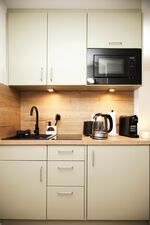 Küche mit Mikrowelle, Herd, Kühlschrank, Wasserkocher, Espressomaschine, Toaster und Kochutensilien