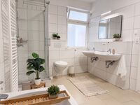 Großzügiges und helles Badezimmer mit Badewanne, Dusche, Handtücher, Toilettenpapier, Seife, Duschgel