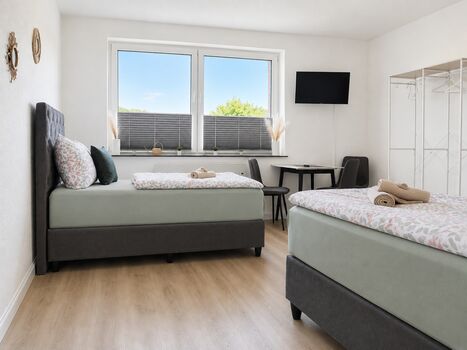 Schlafzimmer3 im 1.OG: Das 3. Schlafzimmer befindet sich auf der rechten Seite am Ende des Flurs und ist der größte Schlafraum im Apartment. Ausgestattet mit drei hochwertigen Einzel-Boxspringbetten bietet es viel Platz und hohen Schlafkomfort.
