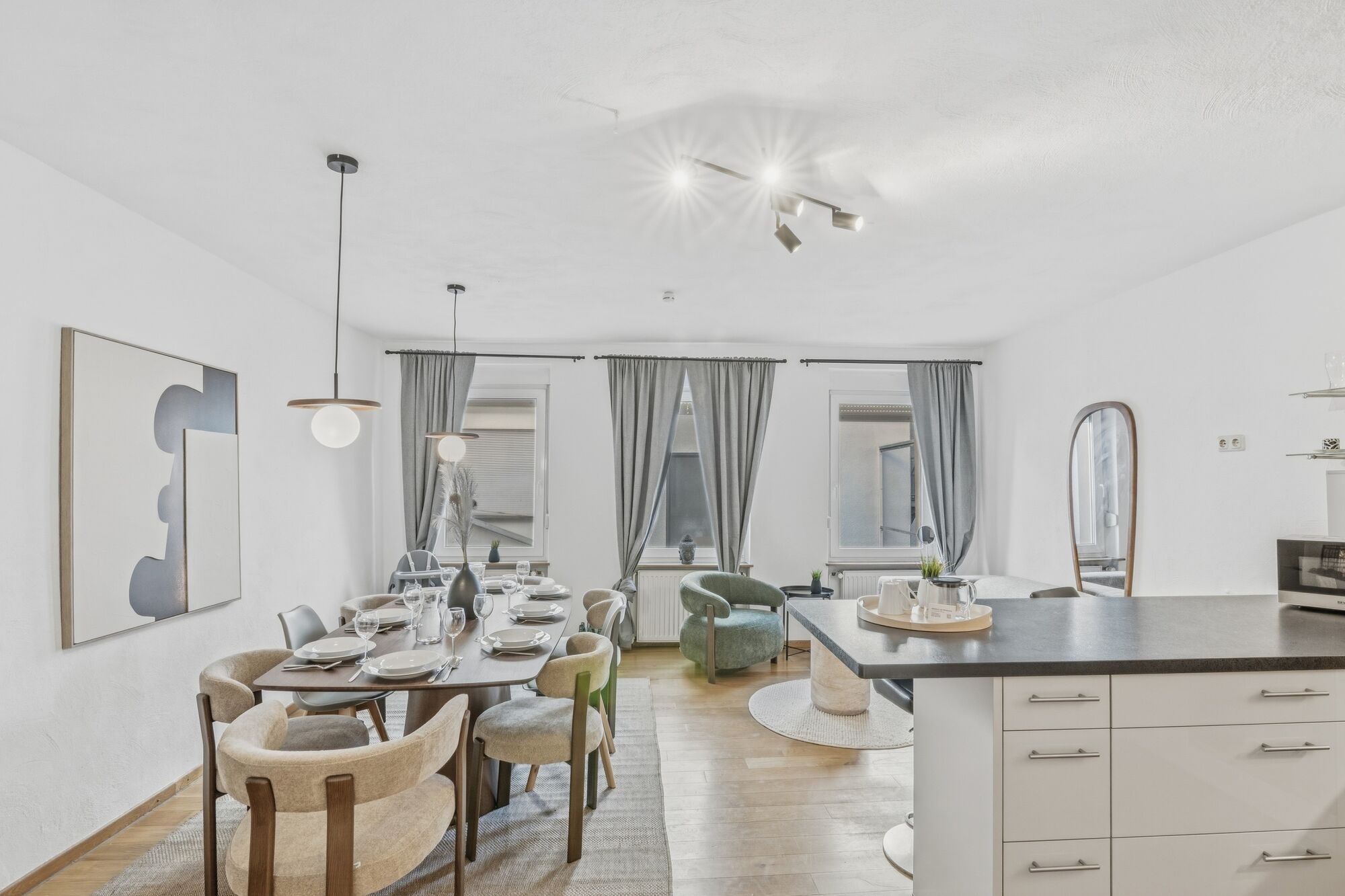 Langer heller Esstisch mit beigen Stühlen, von Hängeleuchten beleuchtet, große Fenster mit Vorhängen