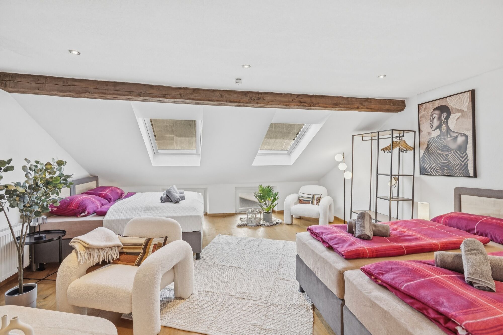 Weitläufiges Dachzimmer mit sichtbarem Holzbalken, vier Betten mit pinker Bettwäsche, zwei Dachfenst