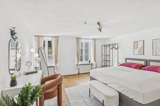 Helles Zimmer mit Doppelbett, braunem Ledersessel und Fenster mit Blick nach außen.