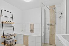 Weißes Badezimmer mit Duschkabine, Badewanne, Handtücher hängen an der Wand.
