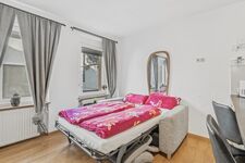 Helles Zimmer mit ausgeklapptem Schlafsofa, pinker Bettwäsche und grauem Vorhang.