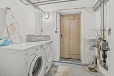 Weiße Einbauwaschmaschine in einem schlichten Hauswirtschaftsraum mit Holztür.