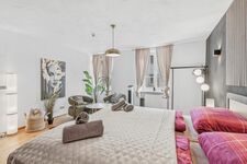 Sitzecke mit zwei grünen Polstersesseln, Hängeleuchte, Wandbild und üppiger Zimmerpflanze.