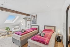 Zwei Einzelbetten mit pinkfarbener Bettwäsche unter einer Dachschräge, Dachfenster lässt Tageslicht 