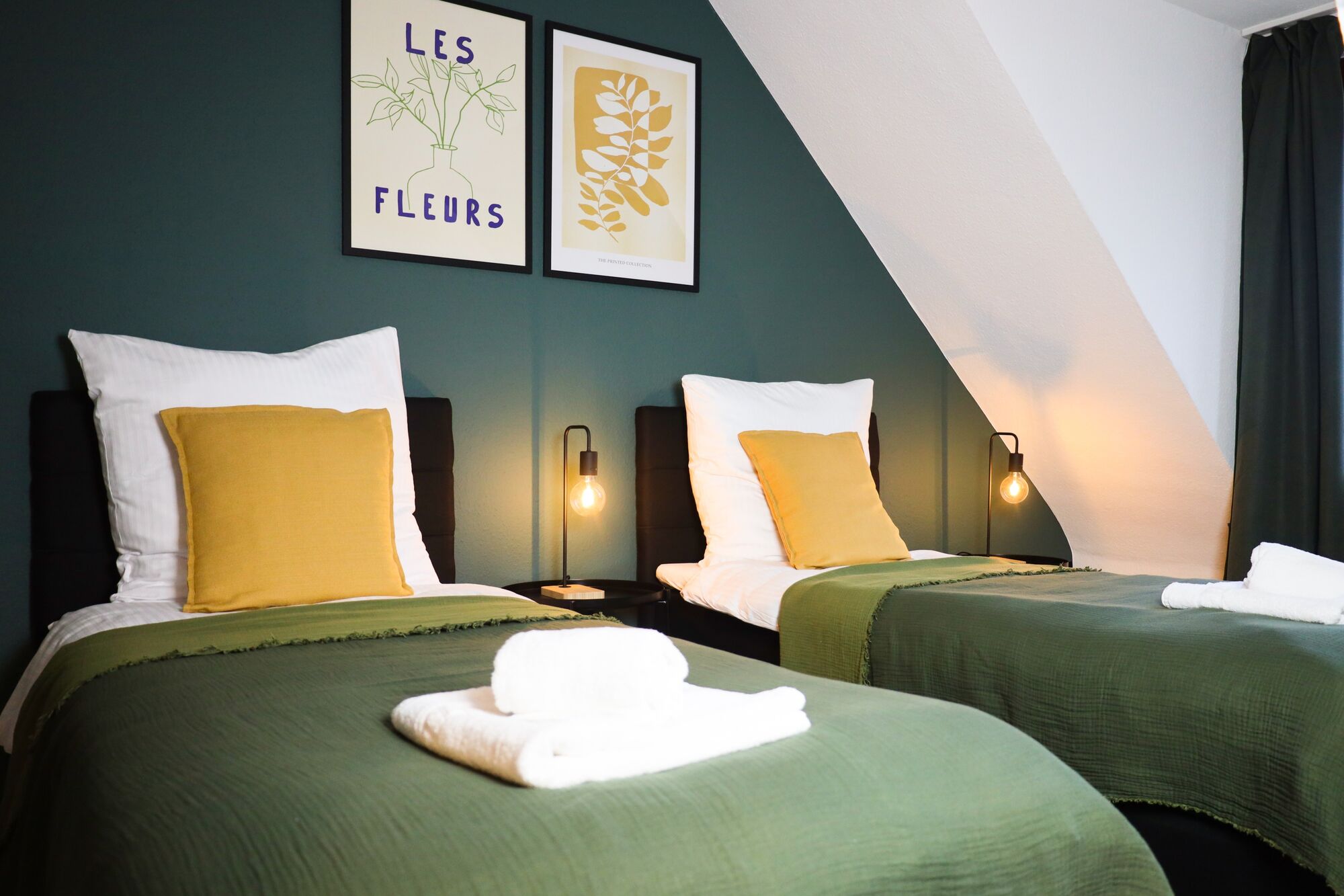 Schlafzimmer 1 - Twin-Schlafzimmer mit zwei Einzelbetten, hochwertiger Bettwäsche, TV, Nachttischlampen und ruhigen Grüntönen.