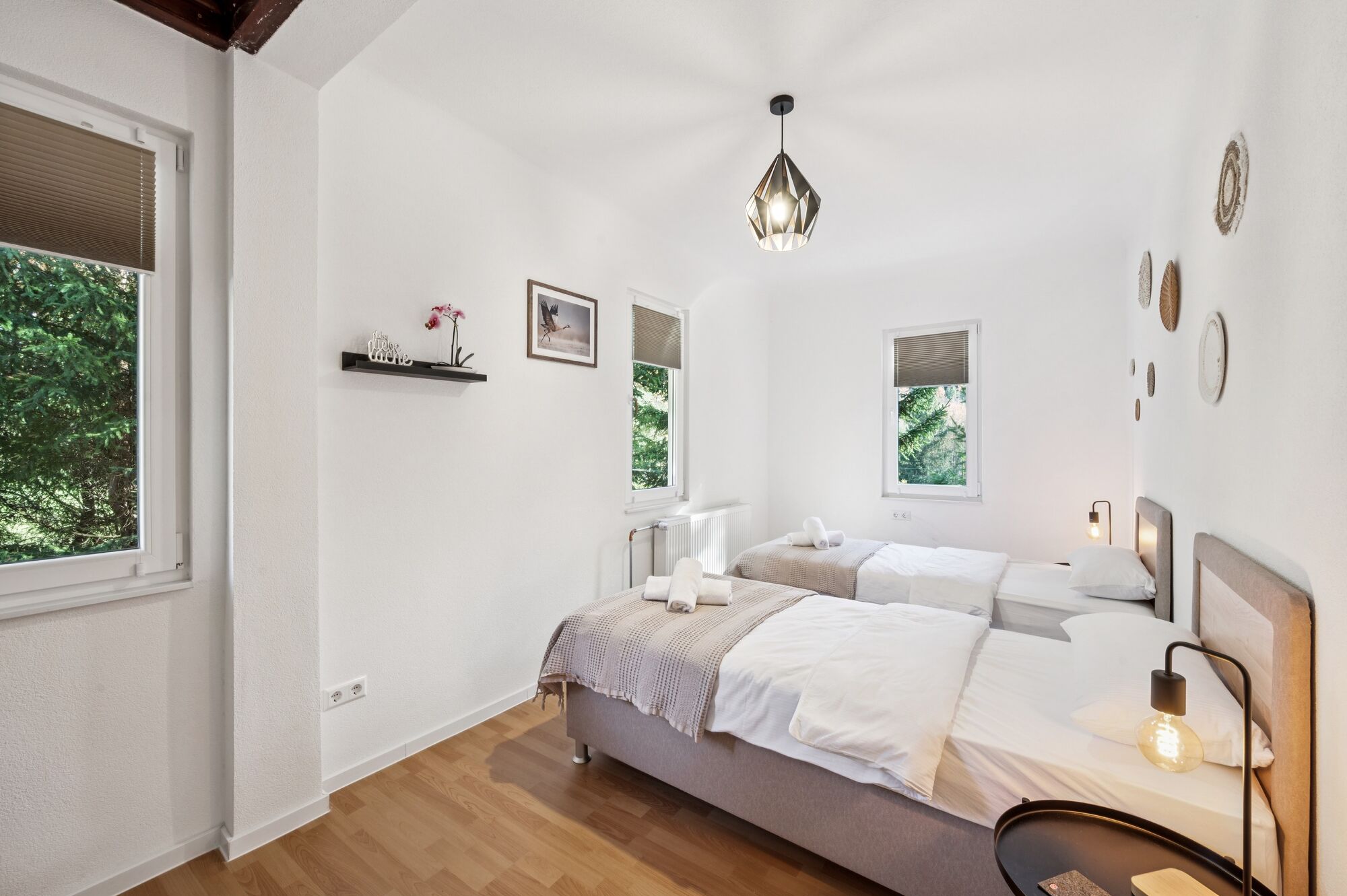 Schlafzimmer 1 mit hochwertigen Boxspringbetten, Nachttischen und einem offenen Kleiderschrank sowie Blick ins Grüne. Die Betten können wahlweise einzeln oder als komfortables Doppelbett gestellt werden.