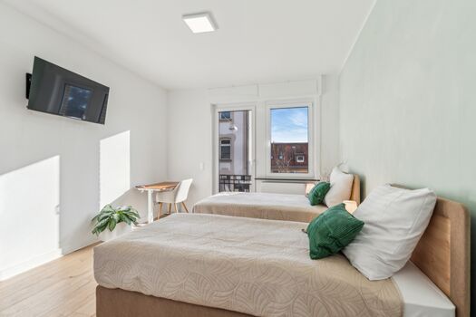 Ein großes Schlafzimmer mit TV und Schreibtisch. Im Hintergrund ist der Ausgang zum Balkon