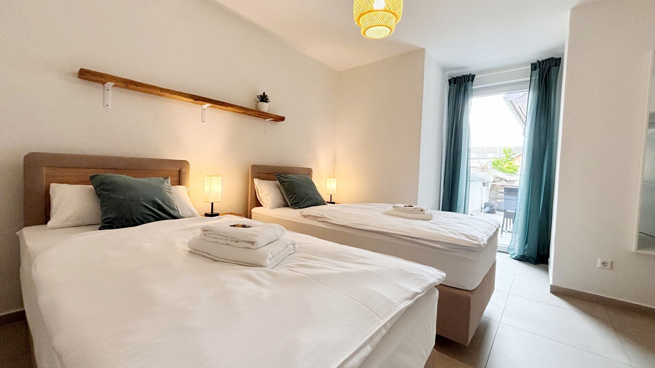 Gemütliches Doppelzimmer mit zwei Einzelbetten, stimmungsvoller Beleuchtung und Zugang zum Balkon. Helle Einrichtung, moderne Deko und ruhige Atmosphäre – perfekt zum Entspannen.