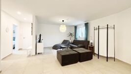 Modernes Wohnzimmer mit gemütlicher Sitzecke, Flachbild-TV und stilvoller Beleuchtung. Helle Fliesen, große Fenster und geschmackvolle Deko sorgen für eine einladende Atmosphäre – ideal zum Entspannen und Wohlfühlen.