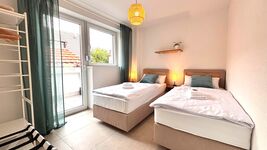 Helles Doppelzimmer mit zwei Einzelbetten, Balkonzugang und gemütlicher Beleuchtung. Modern eingerichtet mit Garderobe, Nachttischen und stilvollen Details – ideal für entspannte Übernachtungen.
