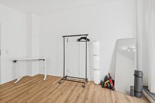 Schwarzer Kleiderständer auf Rollen, weiße Wände, heller Holzboden, viel Platz.