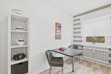 Quadratischer grauer Tisch mit zwei Stühlen, heller Raum mit Zimmerpflanze im Hintergrund.