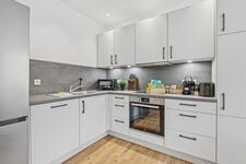 Weiße L-Küche mit grauer Arbeitsplatte, Backofen, Mikrowelle, Fenster mit Grünblick.