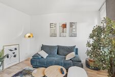 Blaues Sofa mit Kissen, runde Beistelltische, goldene Wandleuchte, heller Holzboden.