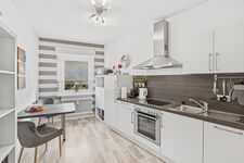 Weiße L-Küche mit grauer Arbeitsplatte, Dunstabzugshaube, Backofen und hellem Holzparkett.