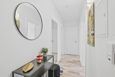 Weißes Bad mit rundem Wandspiegel, schwarzem Waschtisch, Kunstwerk an der Wand, heller Holzboden.